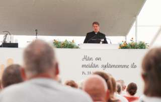 Sakari Typpö puhuu puhujankorokkeella avajaisissa. Etualalla ihmisten takaprofiileja.